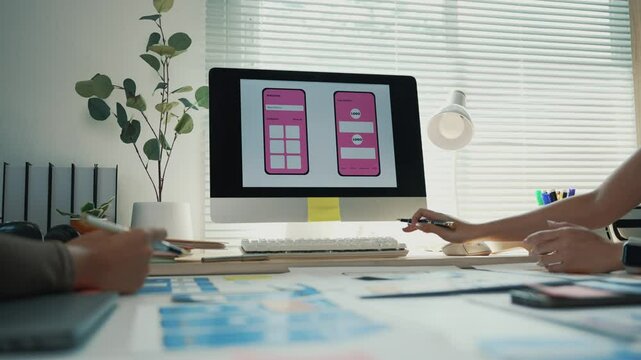 Web designers working together on user interface and user experience of mobile application prototype on desktop computer