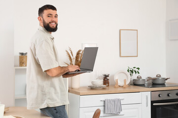 Young bearded man working with laptop in kitchen