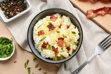 Bowl of tasty potato salad with green onion, bacon and peppercorns on beige background