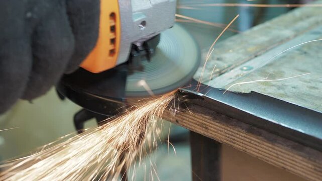 Workshop. A worker removes a layer of metal from a pipe that is clamped to a workbench using a angle grinder.