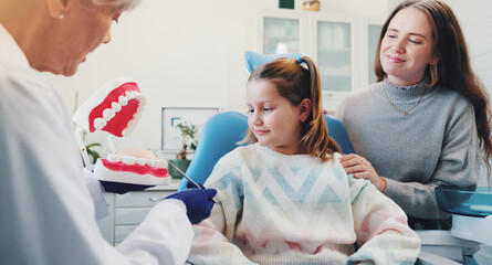 Mom, dentist and child with teeth for teaching, consultation or learning oral hygiene in office with advice. Mother, woman and girl in discussion at clinic with tooth model for dental care education