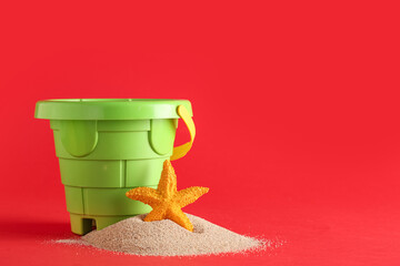 Plastic bucket and sand on red background