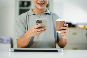 Asian man holding coffee and smartphone, working in modern office with laptop. Perfect for lifestyle,