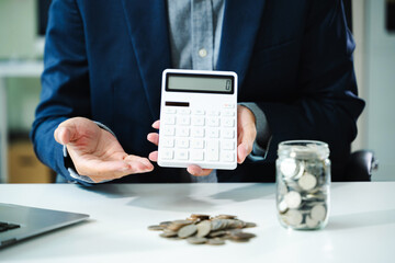 businessman holding coins putting in glass with using smartphone and calculator to calculate...