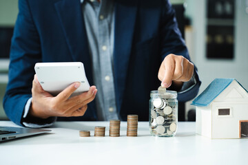 businessman holding coins putting in glass with using smartphone and calculator to calculate...