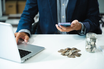 businessman holding coins putting in glass with using smartphone and calculator to calculate...