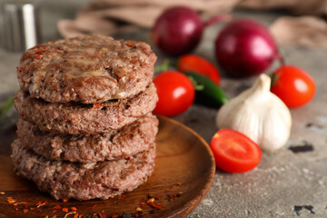 Wooden plate with stack of tasty meat cutlets, vegetables and spices on grey grunge background