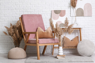Interior of stylish living room with cozy pink armchair, pampas grass and poufs