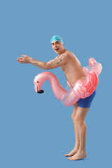 Fototapeta premium Handsome male swimmer with inflatable ring preparing for jump on blue background