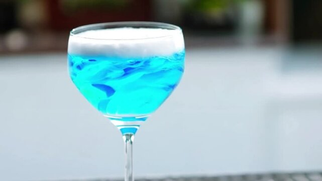 The foam cocktail is the epitome of the image of the ocean. Elegant blue cocktail with a frothy white foam and swirling colors in a martini glass.