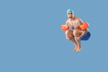 Handsome male swimmer with inflatable armbands doing cannonball jump on blue background
