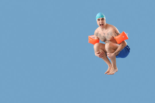 Handsome male swimmer with inflatable armbands doing cannonball jump on blue background - Powered by Adobe