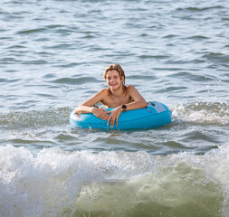 A cheerful young girl swims with an inflatable circle in the sea