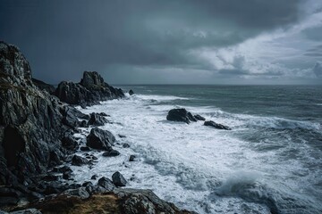 Fototapeta premium Dark stormy coastline with jagged black rocks and crashing foamy waves.