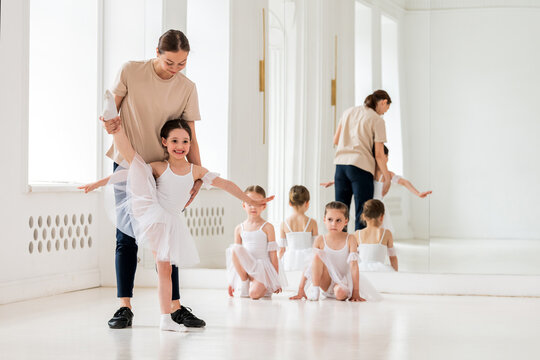 ballet teacher helps a girl in a white tutu perform an element