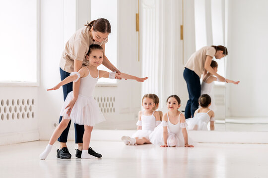 ballet teacher helps a girl in a white tutu perform an element