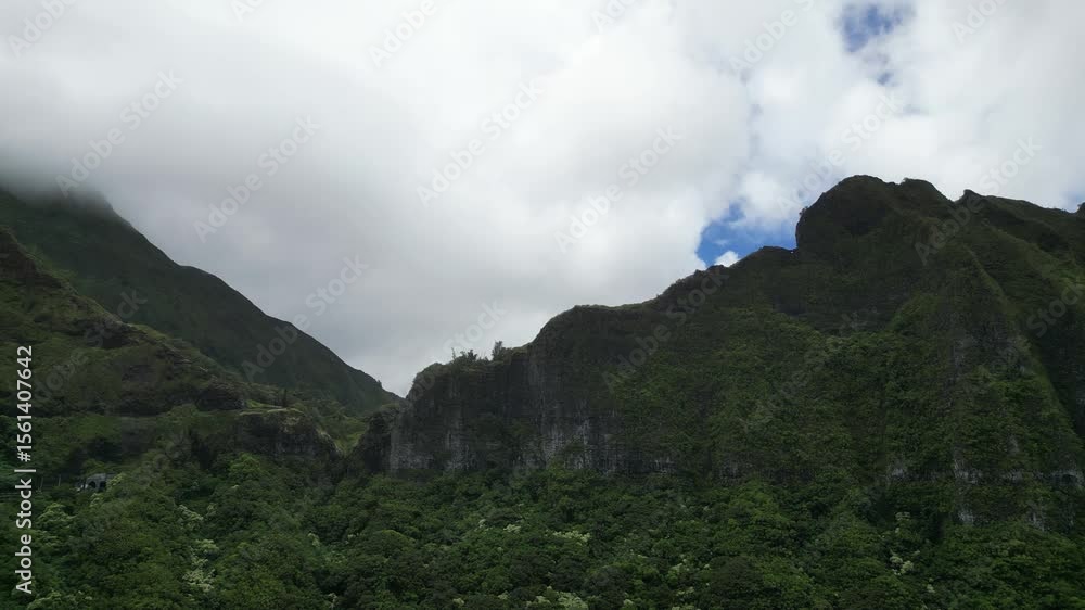 Poster drone captures hawaii’s forested mountains from below with cloudy sky and steep cliffs.