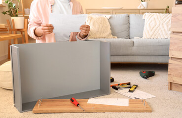 Man with instructions assembling chest of drawers at home