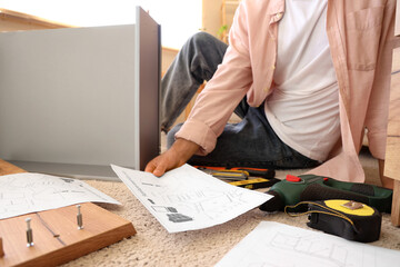Man with furniture plan assembling chest of drawers at home