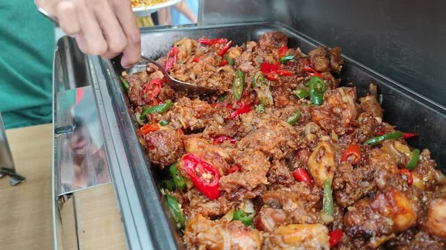 Cinematic footage of a buffet spread featuring classic Asian dishes, including stir-fried noodles (mie goreng) and spicy seasoned chicken (ayam bumbu pedas). The food is presented in stainless steel 