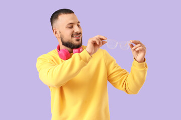 Handsome young man with headphones and eyeglasses on lilac background