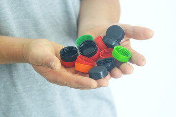 Sustainability and reuse: a man holds multi-colored plastic bottle caps in his folded palms, close-up photo. Concepts of eco-awareness, minimalist living and reducing plastic waste in everyday life