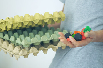 Zero waste habits in daily life: a person holds plastic bottle caps and stackable cardboard egg trays. Sustainable living, mindful sorting and home recycling solutions for environmental responsibility