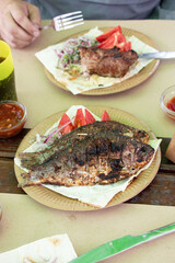 Fried river fish on the grill and shashlik with vegetables in a street cafe, traditional food on a paper plate