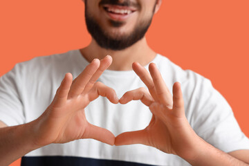 Thankful young man making heart gesture on orange background