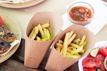 Fried potato strips and tomato salad on a wooden table in a street cafe, food