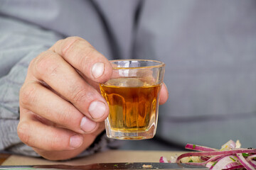 Man holding shot glass of alcohol at table in street cafe during lunch, shot glass of cognac