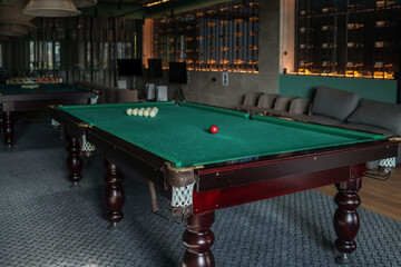 Cozy billiard room featuring classic green-felt pool tables; red and white balls arranged for play...