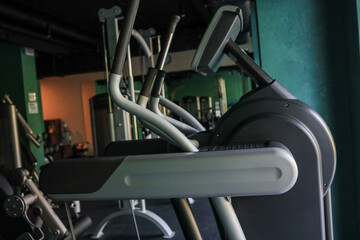 Side view of Technogym elliptical trainer in a dimly lit hotel fitness room with teal walls and other machines in the background, ready for a cardio session, no people present