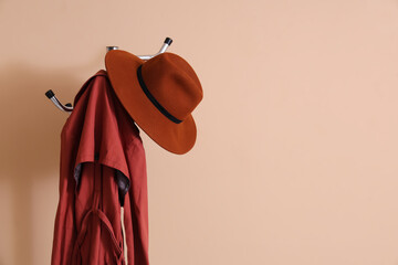 Rack with coat and felt hat near beige wall