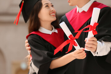 Couple of graduating students with diplomas hugging outdoors, closeup