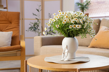 Vase with chamomiles and statuette on table in living room
