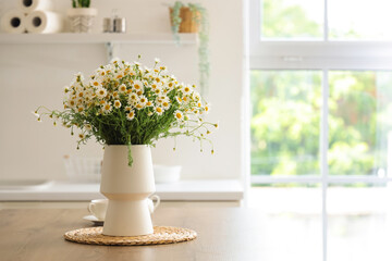 Vase with chamomiles on table in kitchen