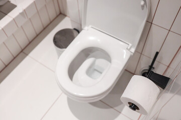Top-view modern hotel WC with pristine ceramic bowl, open lid, wall-mounted tissue roll and small...