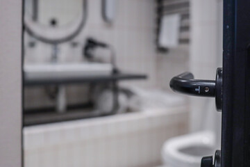 Close-focus shot of black door handle with modern hotel bathroom softly blurred behind—oval...