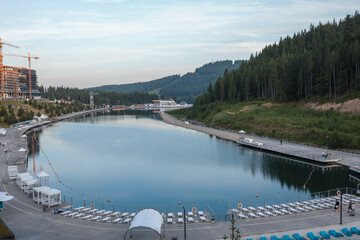Wide view of tranquil mountain lake reflecting pine-clad slopes and soft evening sky, with...