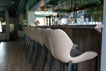 Row of beige leather bar stools along a wooden counter in a stylish modern lounge bar; low-angle...