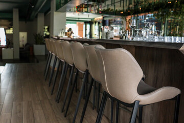 Row of beige leather bar stools along a wooden counter in a stylish modern lounge bar; low-angle perspective highlights sleek interior design and inviting ambience