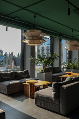 Sun-lit hotel lounge with panoramic windows, grey modular sofas, rustic oak tables, sculptural...