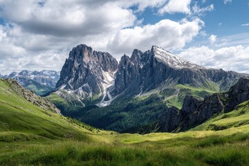 Obraz premium Dramatic alpine vista; verdant valley, towering rocky peaks partially snow-capped under a partly cloudy sky