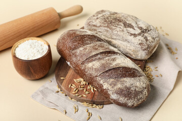 Board with loaves of fresh bread, flour and wheat on beige background