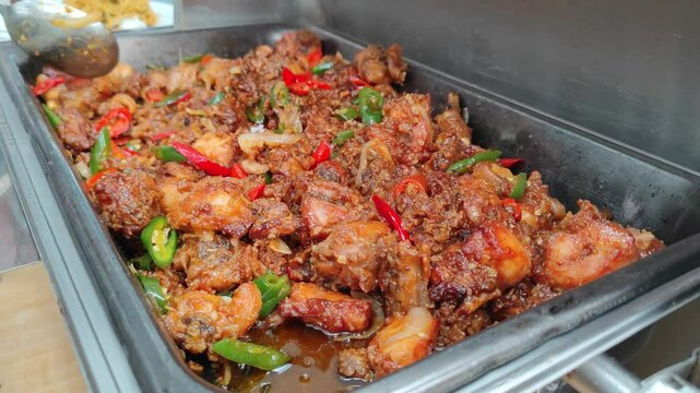 Cinematic footage of a buffet spread featuring classic Asian dishes, including stir-fried noodles (mie goreng) and spicy seasoned chicken (ayam bumbu pedas). The food is presented in stainless steel 