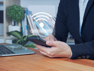 Wireless network password security concept with businessman holding smartphone and laptop on wooden desk in office