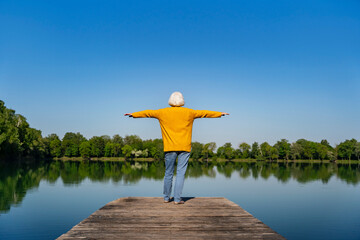 Woman standing on a jetty by the lake with arms outstretched enjoying nature