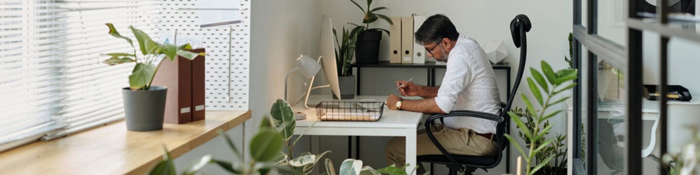 Businessman working at a desk in a modern office with plants and natural light