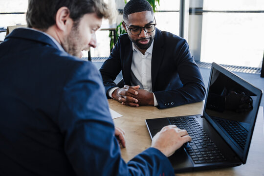 Businessman explaining contract procedures to client on laptop in office